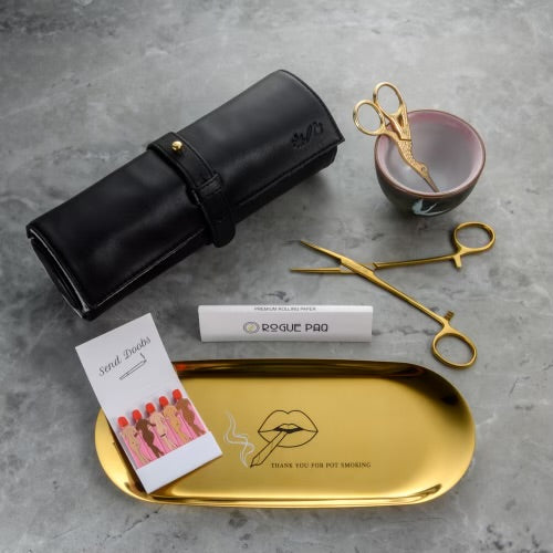 Cute smoking accessories by Rogue Paq. This shot features the Thank You for Pot Smoking rolling tray, a book of best selling SendNudes Send Doobs matches, a book of all natural hemp rolling papers, hemostats joint clips, the signature Rogue Paq Ritual Case in lambskin leather, and the Crane Manual Grind Set.