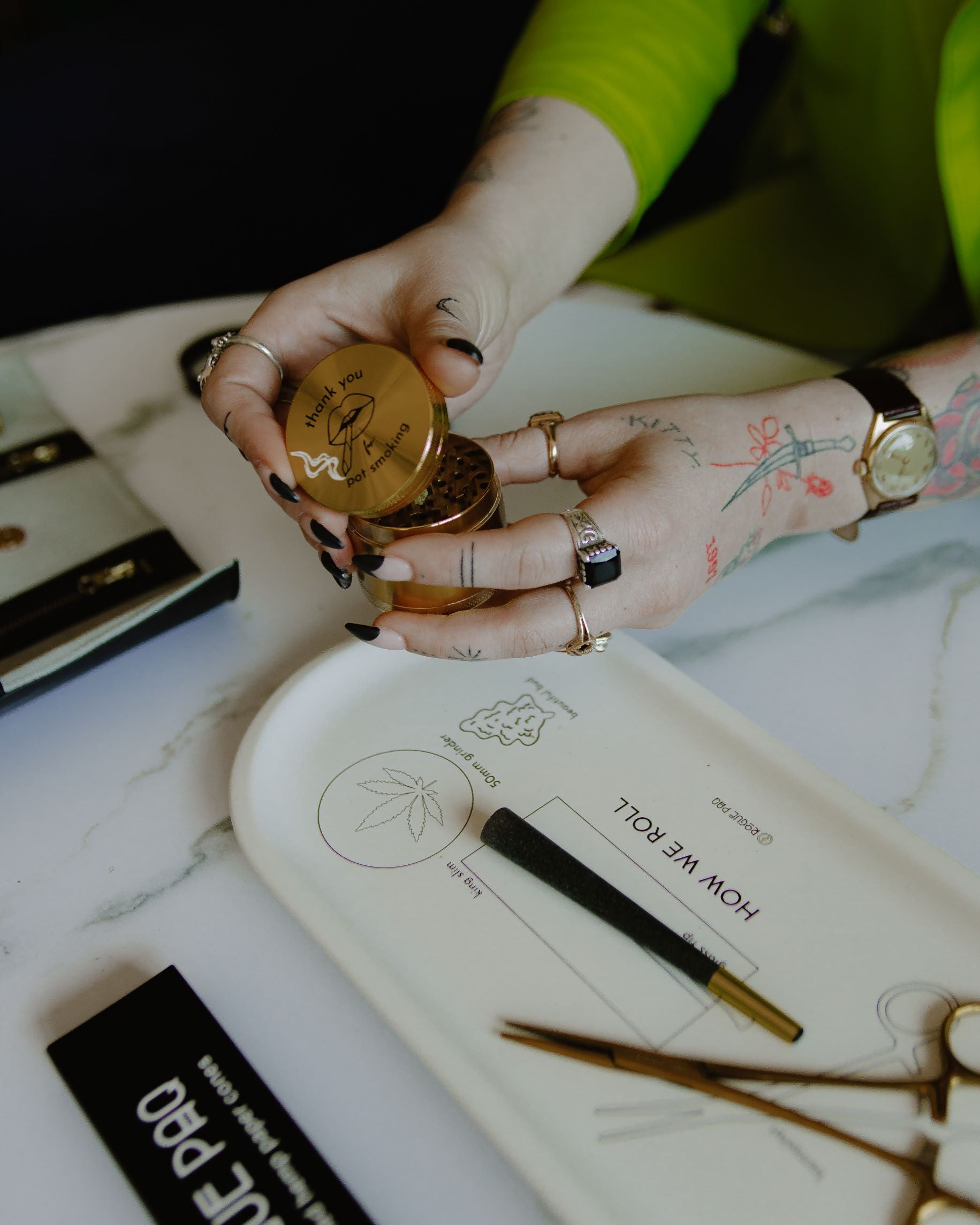 Thank you for pot smoking grinder is being opened by the model. Theis shot shows the grinder was designed for the connoisseur who appreciates a bit of wit with their ritual. She is using the grinder with the Rogue Paq How We Roll rolling tray, hemp cones, and hemostat joint clips.
